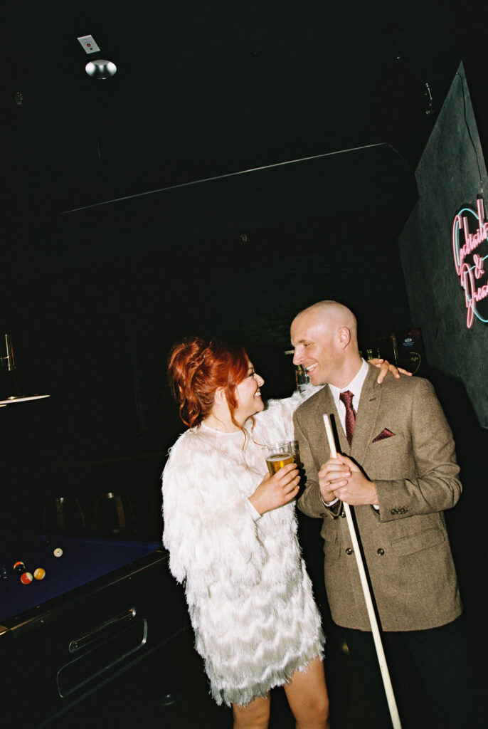 Bride and groom posing for photos while playing pool