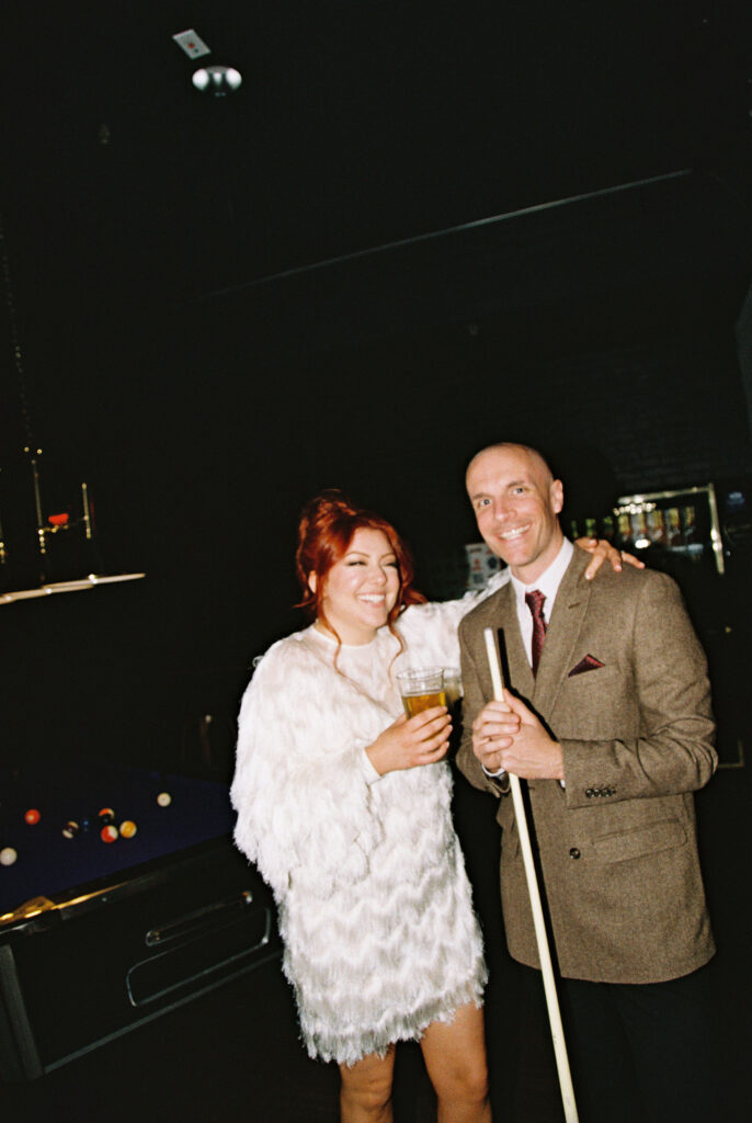 Bride and groom posing for photos while playing pool