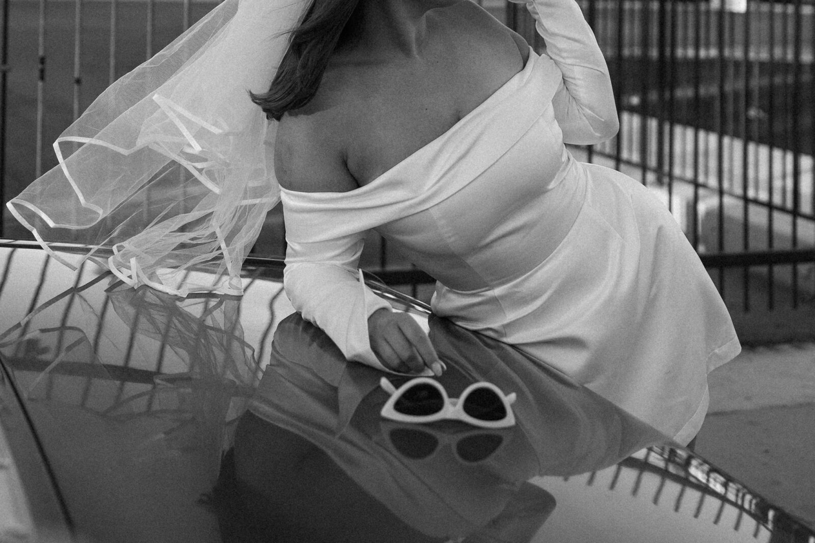 Black and white close up photo of a woman leaning against a vintage car