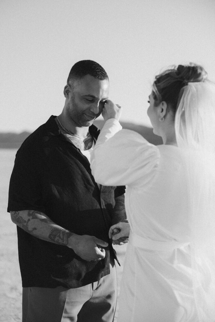 Black and white photo of a bride wiping away grooms tears during their emotional vows exchange 