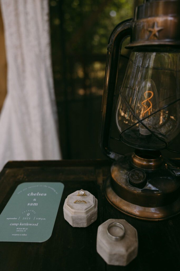 Summer camp wedding details with invites, rings, and a lantern