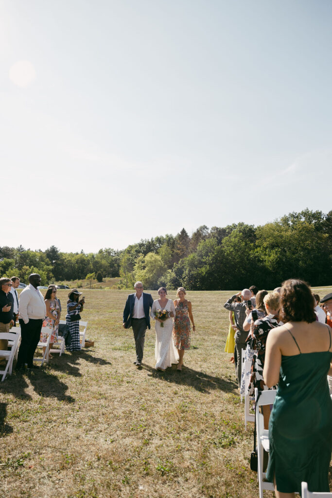 Bride being walked down the aisle by her parents for her summer camp wedding ceremony at Camp Kettlewood in Wisconsin