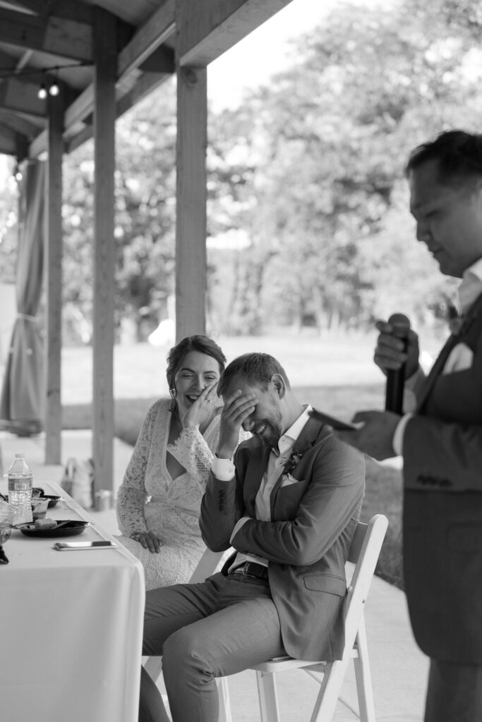 Black and white candid photo of a bride and groom laughing during wedding speeches