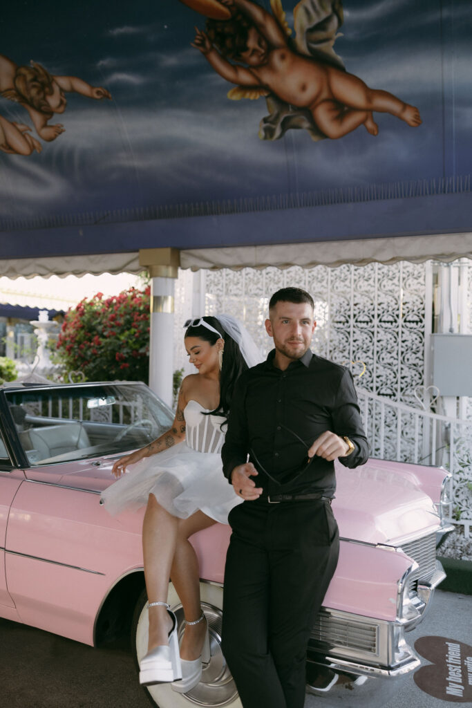 Bride and groom sitting on the Pink Cadillac at The Little White Wedding Chapel for their Las Vegas elopement photos