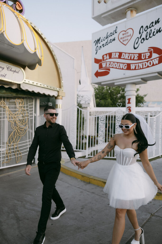 Bride and groom walking in front of The Little White Wedding Chapel and holding hands