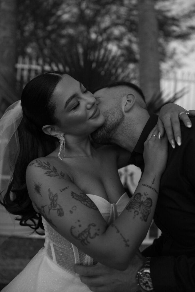 Black and white photo of a man kissing his bride on the neck