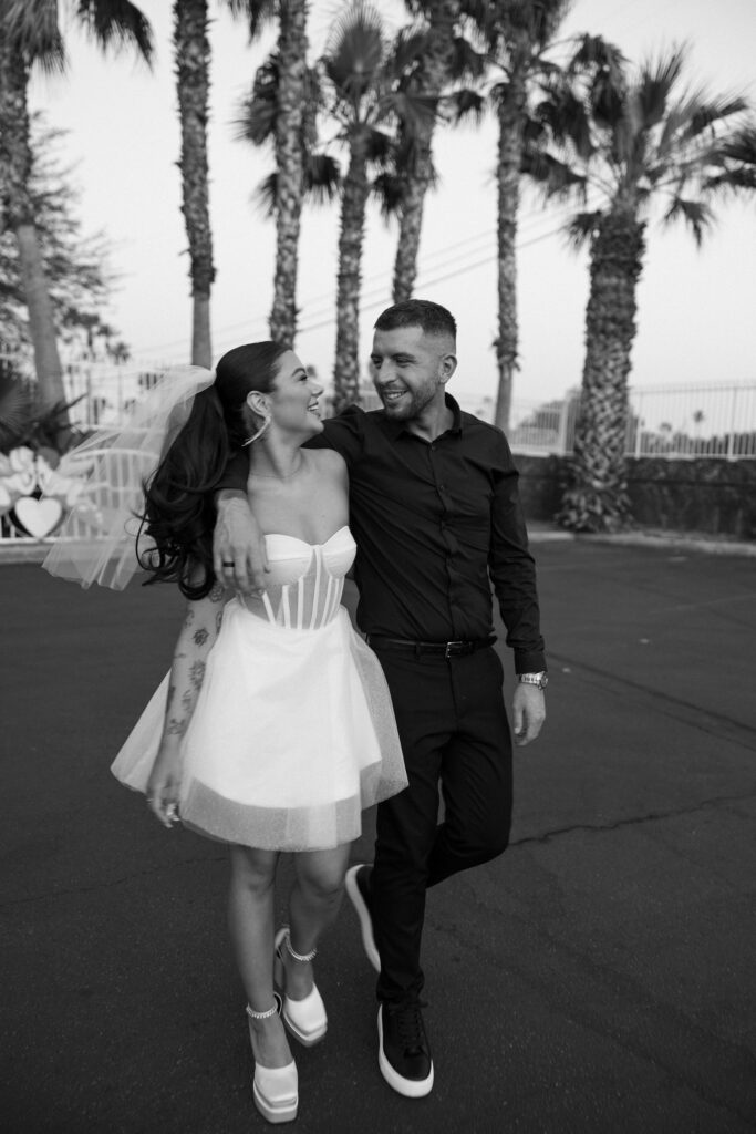 Black and white candid photo of a bride and groom walking in a parking lot