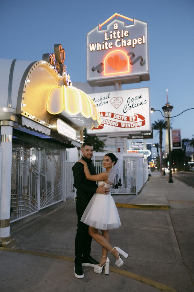 Bride and groom posing for photos at night in front of The Little White Wedding Chapel sign