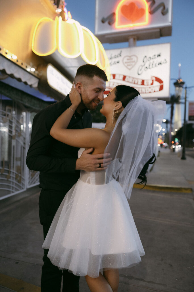 Bride and groom posing for photos at night in front of The Little White Wedding Chapel sign