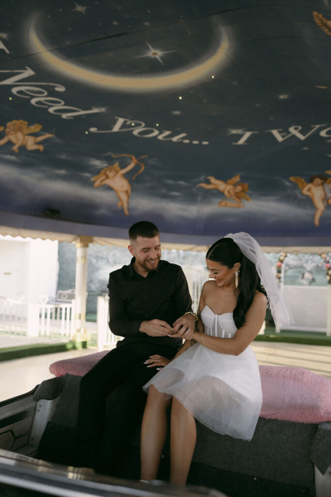 Groom putting the ring on his brides hand during their Las Vegas elopement in the Pink Cadillac of Little White Wedding Chapel