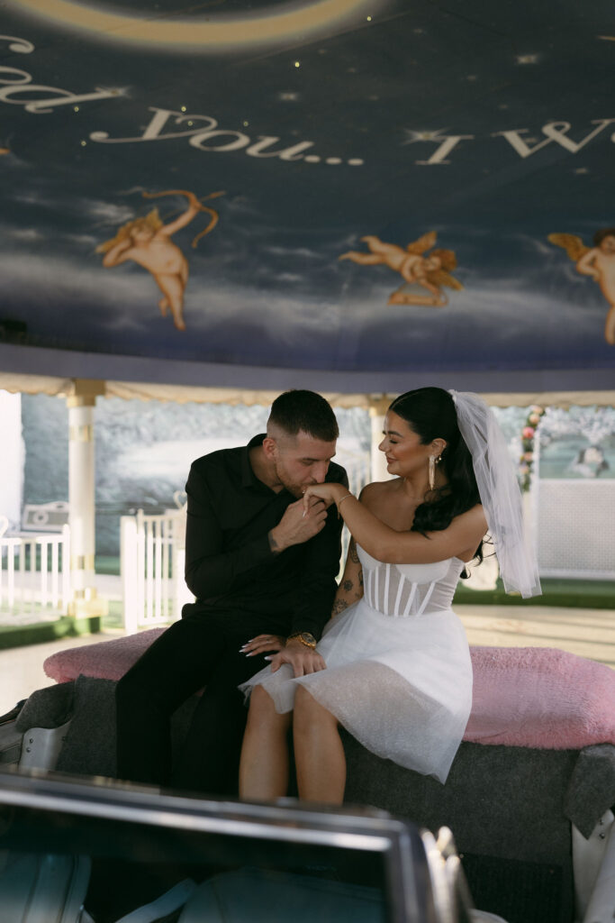 Groom kissing his brides hand during their Pink Cadillac Ceremony at Little White Wedding Chapel in Las Vegas