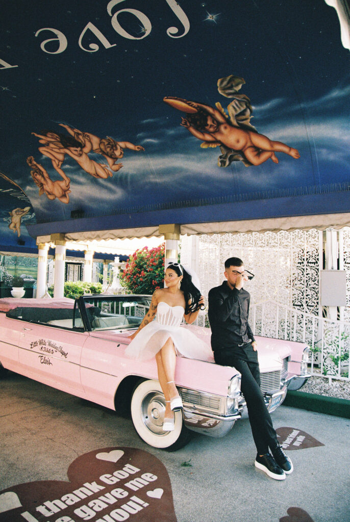 Editorial elopement photo of a bride and groom sitting on the Pink Cadillac on film