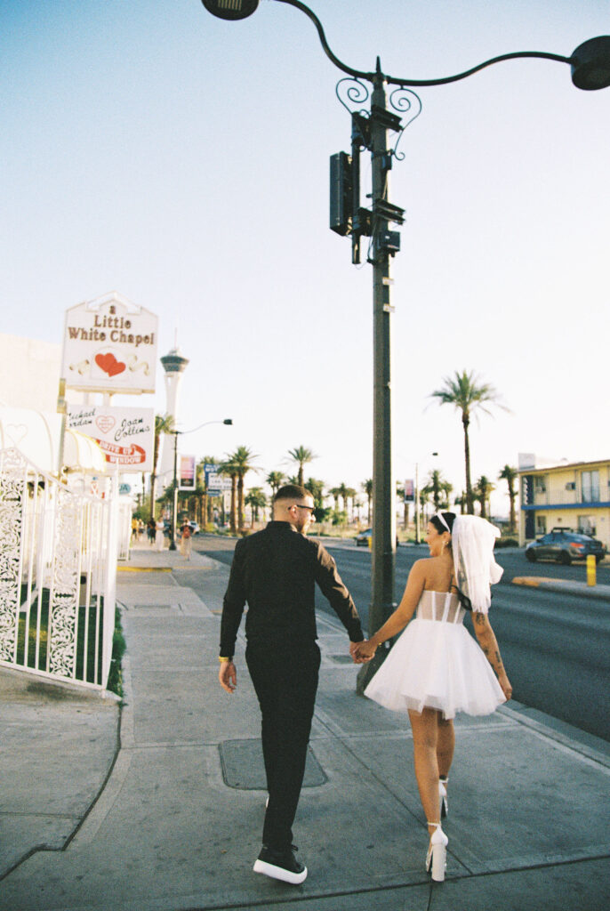 Bride and groom holding hands as they walk on the sidewalk captured on film