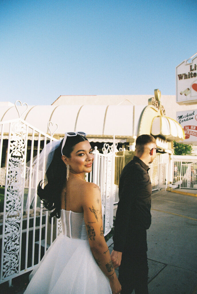 Bride and groom holding hands as they walk on the sidewalk captured on film