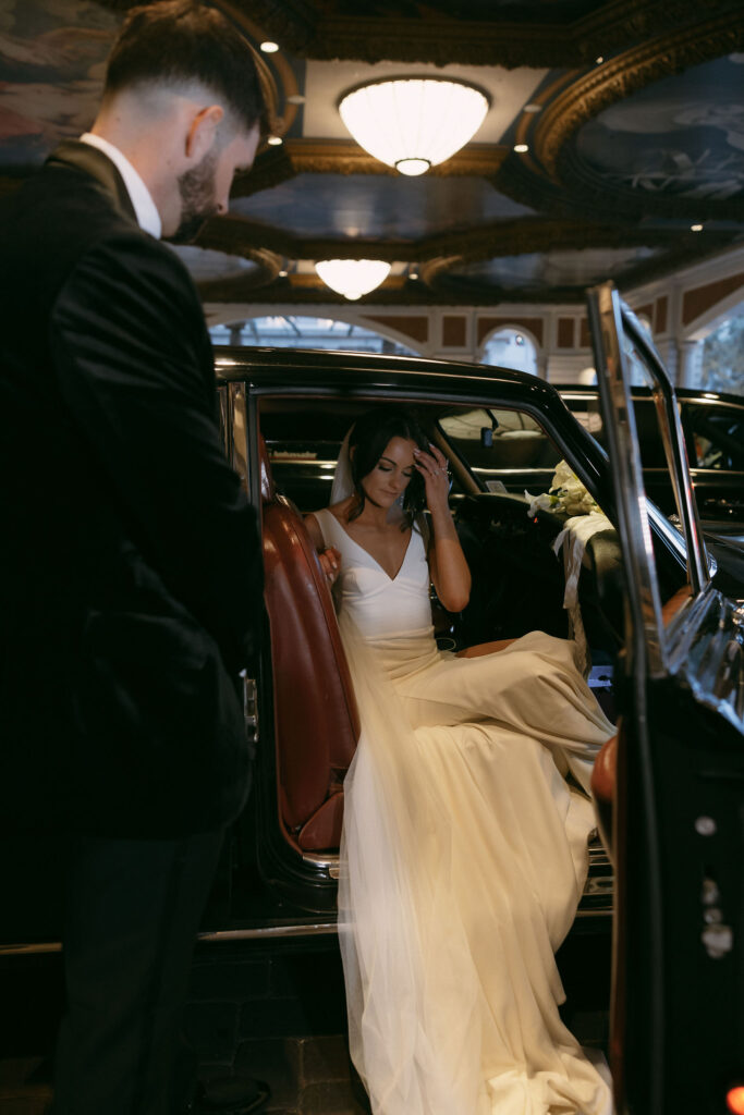 Groom helping his bride step out of their Rolls-Royce after their wedding