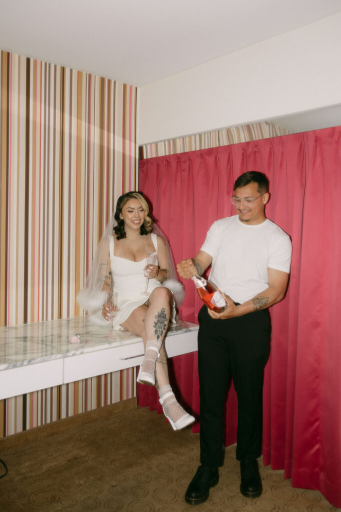 Bride and groom popping champagne in their Flamingo Hotel room