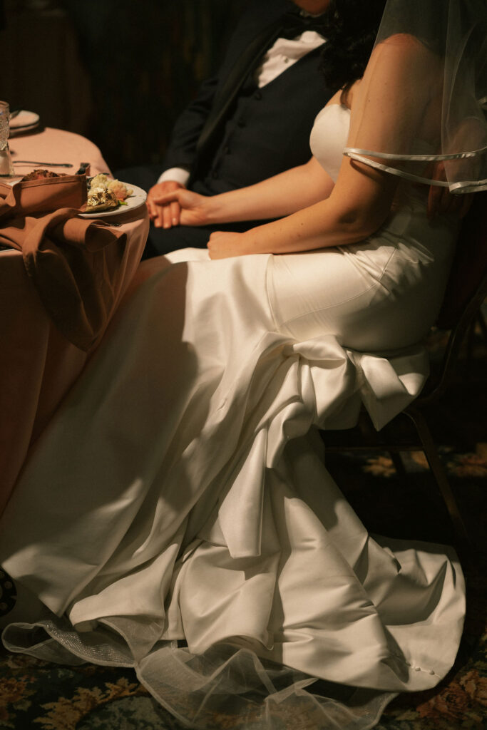 Close up shot of a bride and groom holding hands during speeches at their Madonna Inn wedding reception