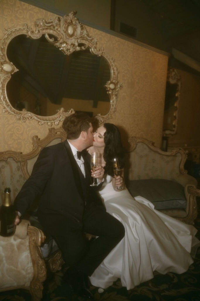 Bride and groom kissing while holding champagne glasses