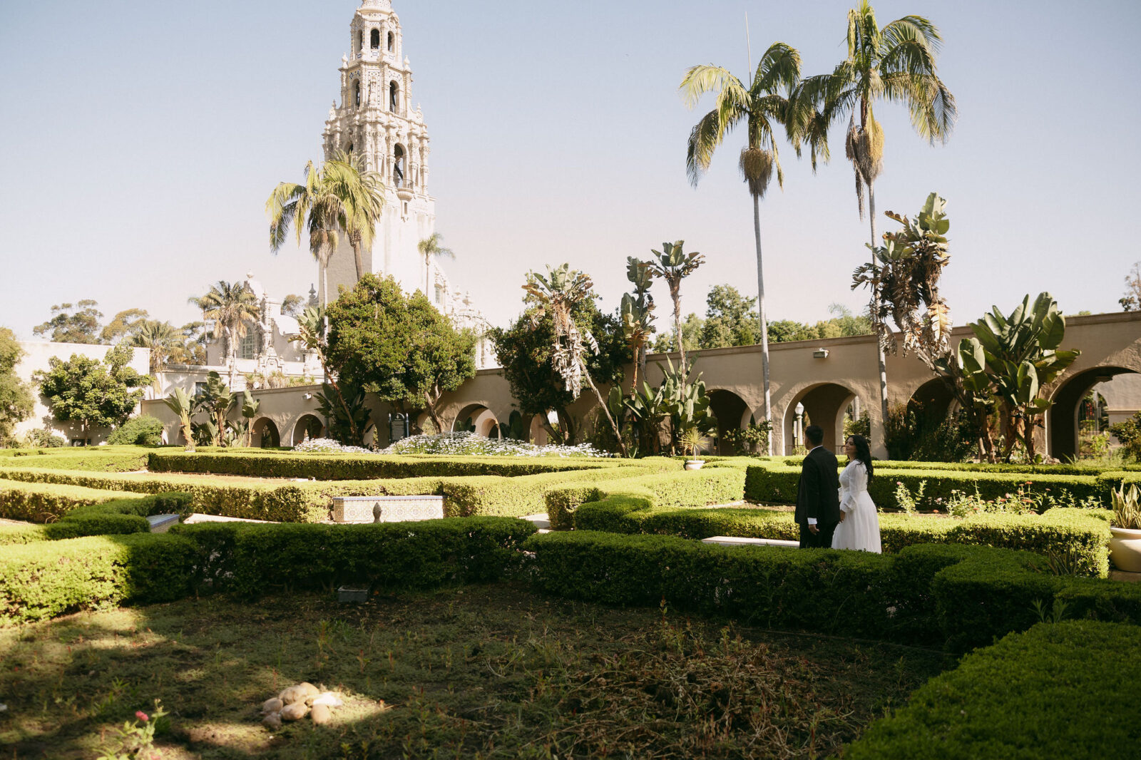 Couples walking through Alcázar Garden for their Balboa Park engagement photos