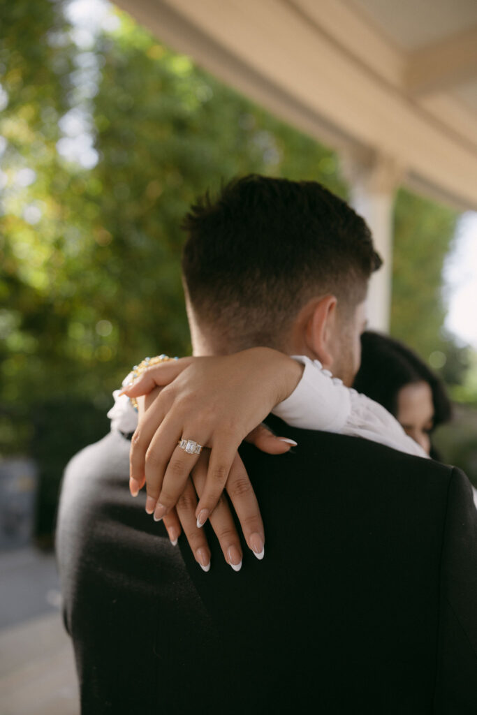 Woman wrapping her arms around her fiancés neck and showing off her engagement ring