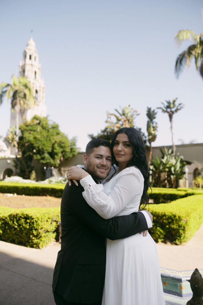 Couple holding each other during their Balboa Park engagement photos with the California Tower in the background