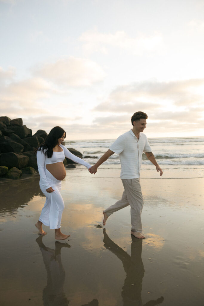 Man and woman walking along the beach for their San Diego maternity photos