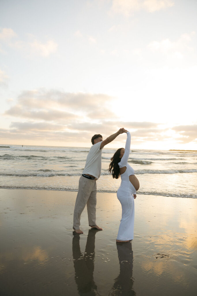 Man twirling his pregnant wife on the beach