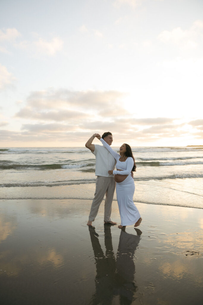 Man twirling his pregnant wife on the beach