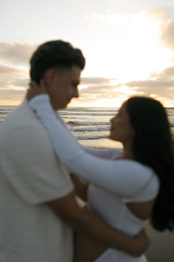 Man and woman embracing each other on the beach during sunset for their San Diego maternity photos