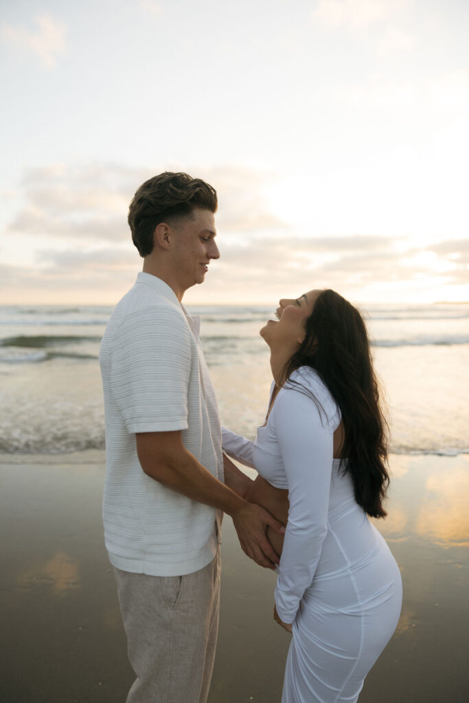 Man holding his wifes pregnant belly during their couples San Diego maternity photos on the beach