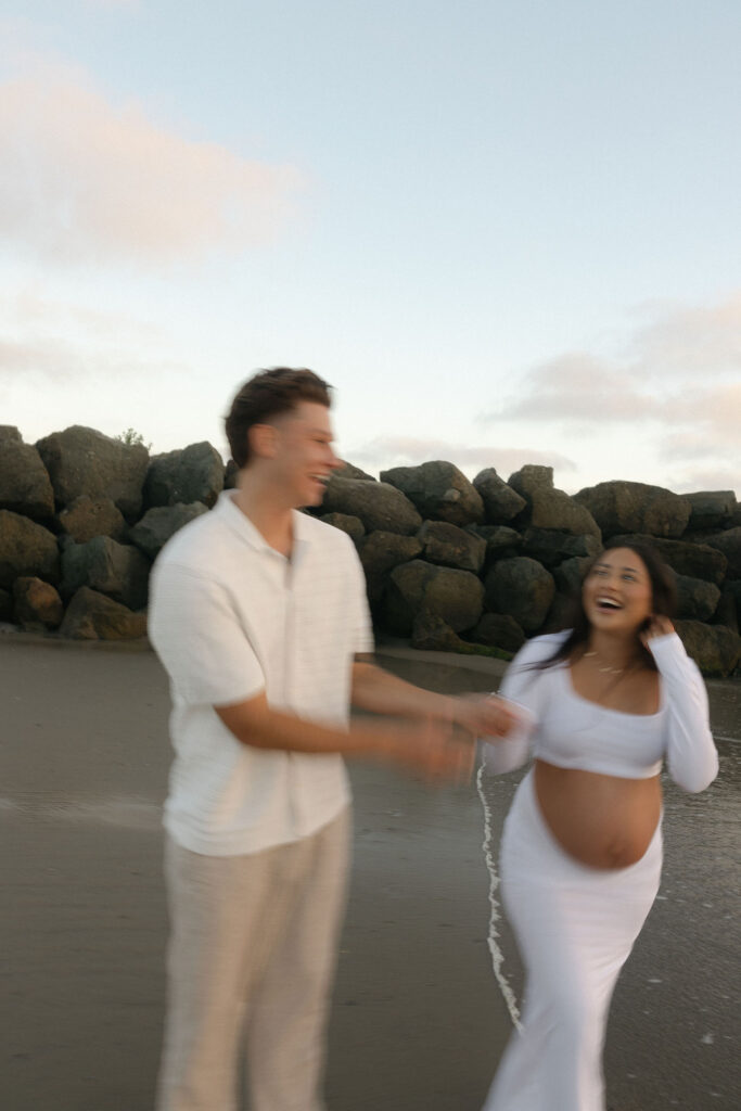 Man and woman laughing during their couples beach maternity photos