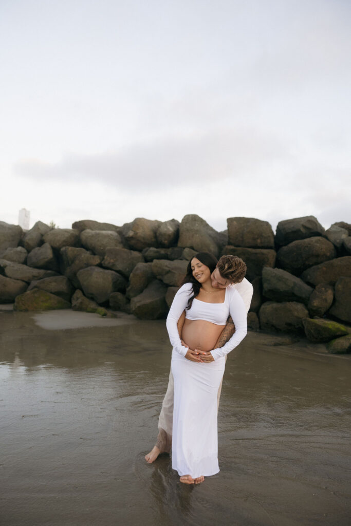 Man and woman posing for their San Diego maternity photos on the beach