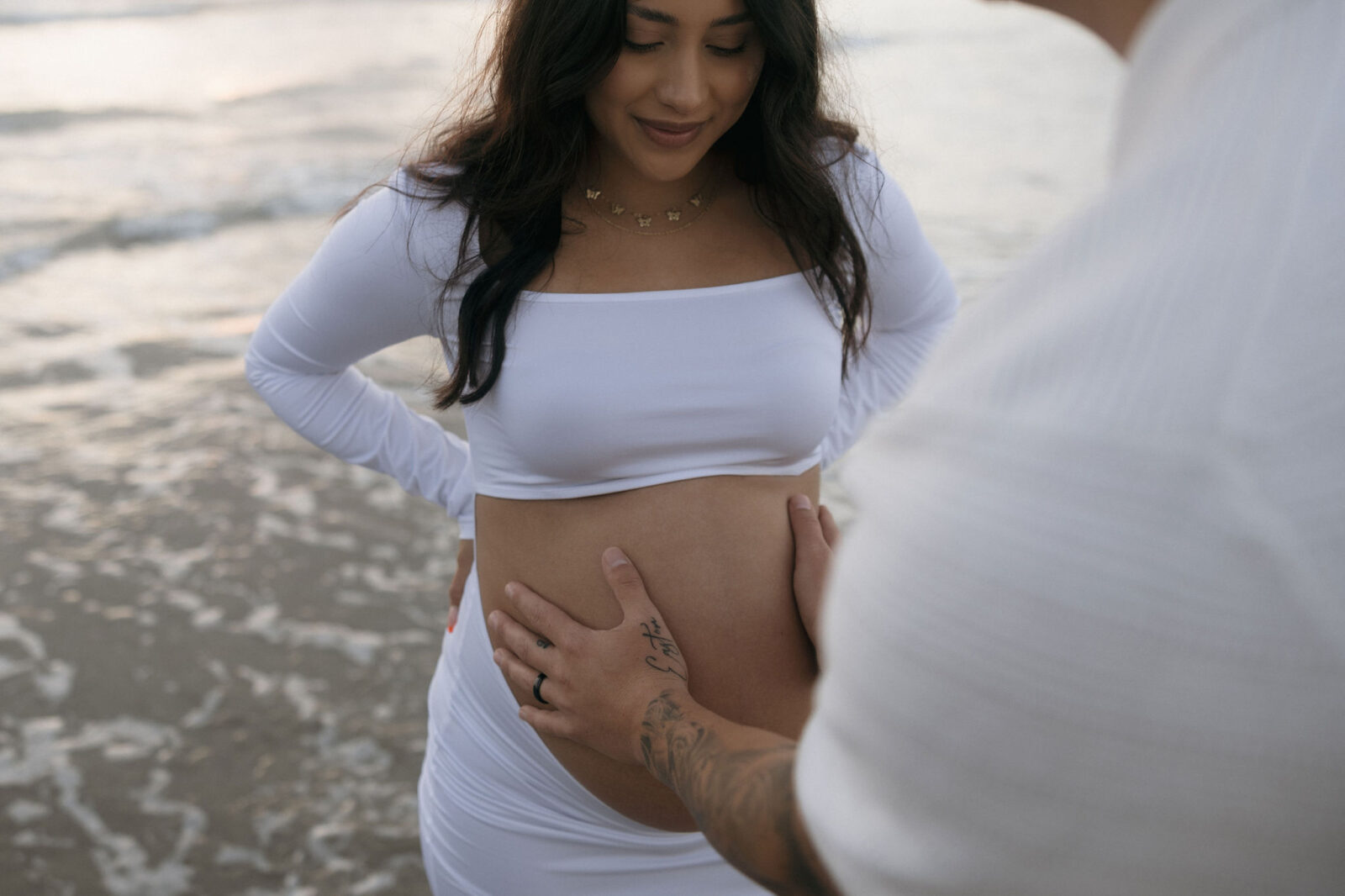 Close up of a man holding his pregnant wives belly during their couples beach maternity session