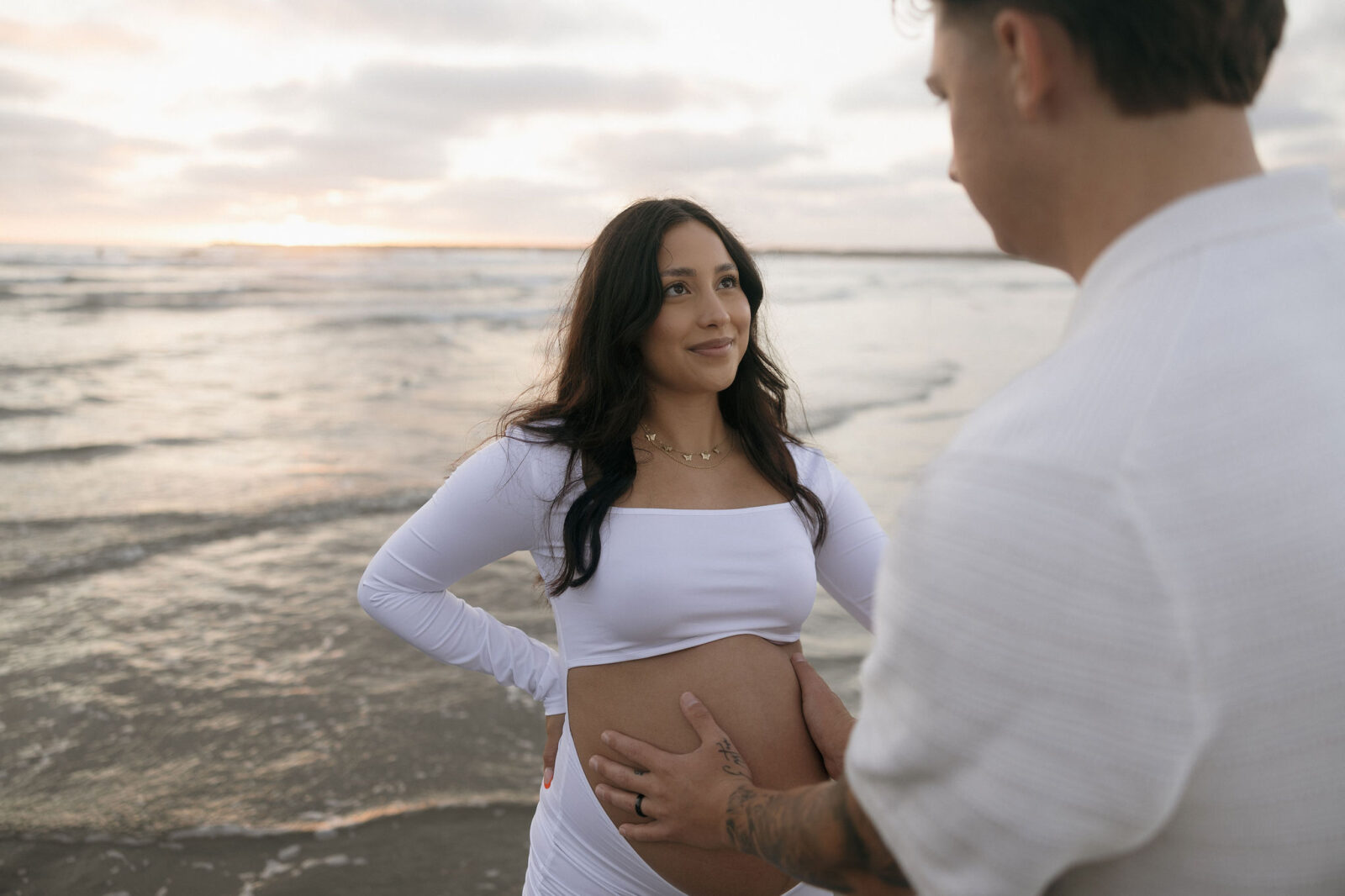 Man and woman posing for their San Diego maternity photos on the beach at sunset