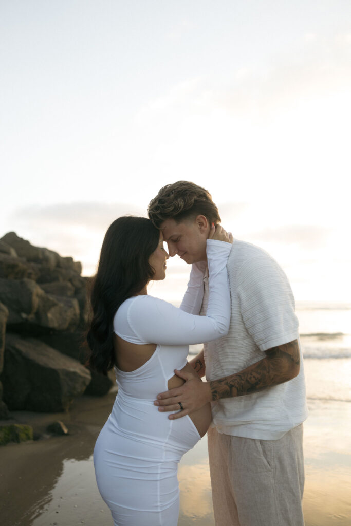 Man and woman posing for their San Diego maternity photos on the beach