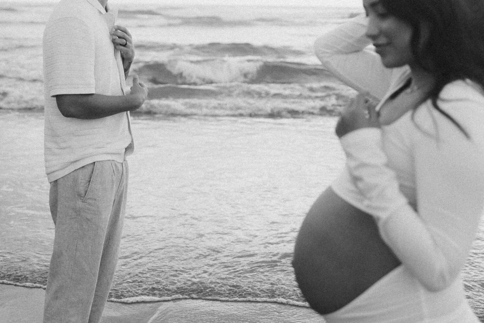 Black and white close crop photo of a man and pregnant woman on the beach