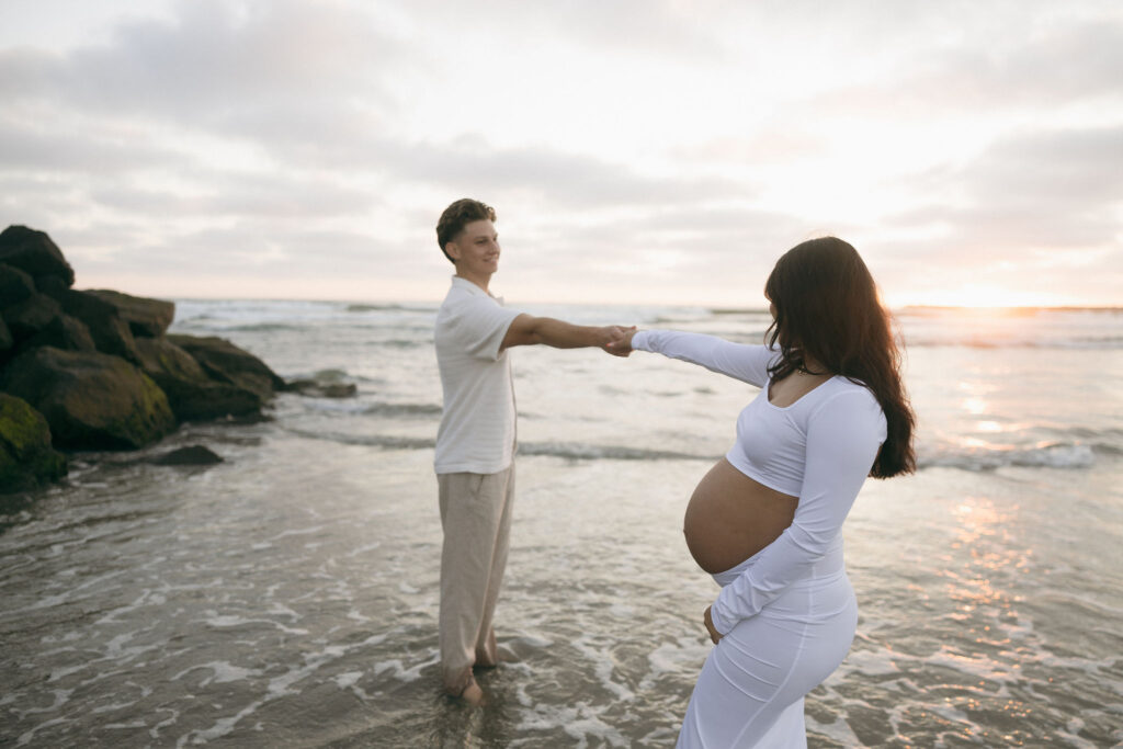 Man and woman holding hands during their San Diego maternity photos at sunset