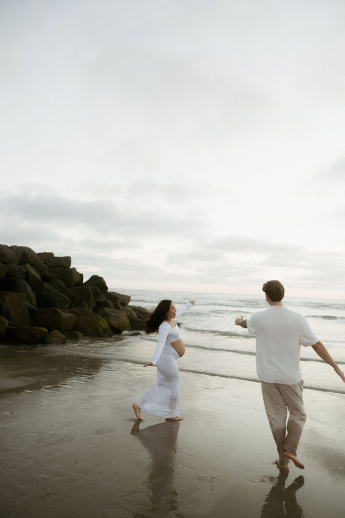 Man and woman running on the beach for their San Diego maternity photos