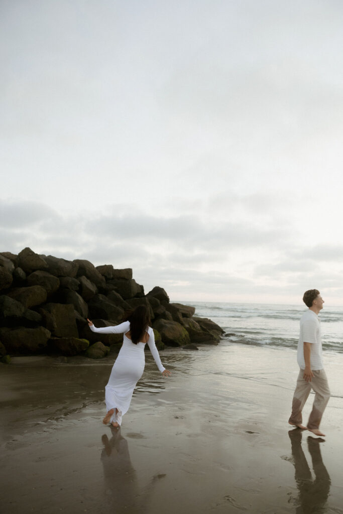 Man and woman running on the beach for their San Diego maternity photos