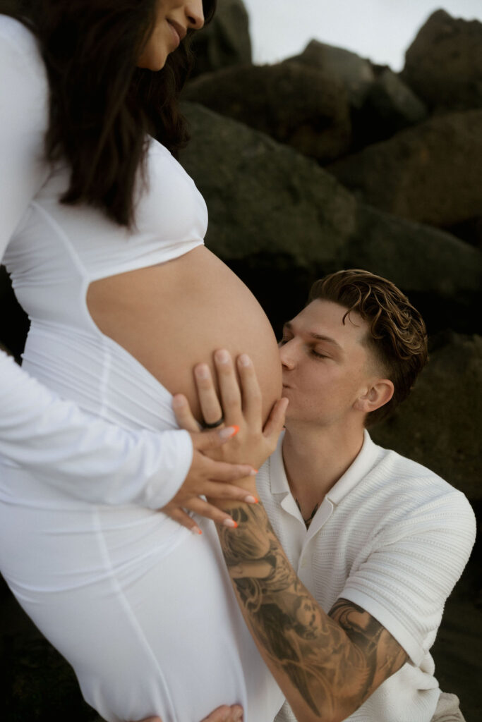 Man kissing his wifes pregnant belly during their San Diego maternity photos