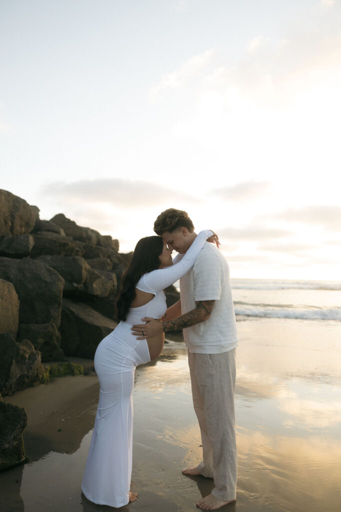 Man and woman posing for their San Diego maternity photos on the beach