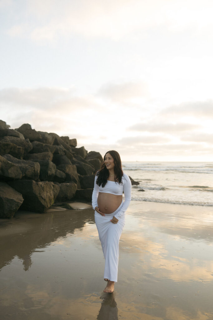 Woman walking along the beach for her San Diego maternity photos