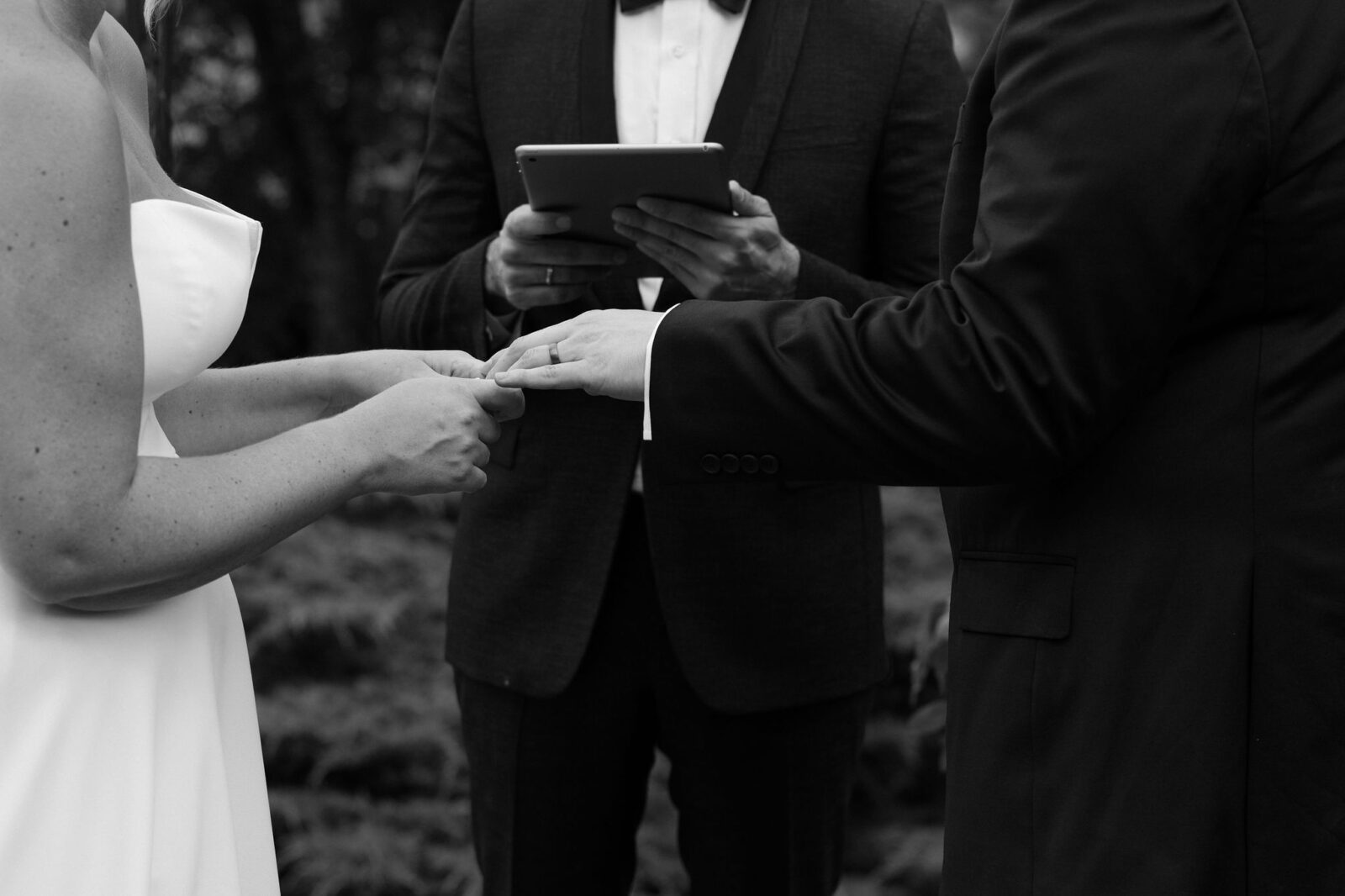 Black and white photo of a bride and groom exchanging rings during their ceremony