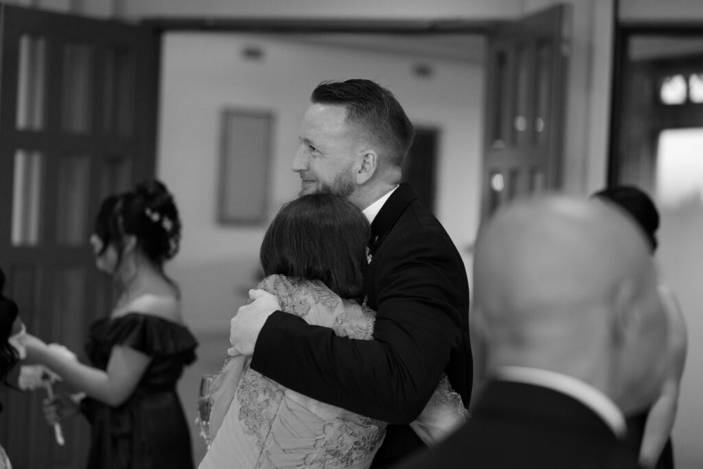 Black and white photo of a groom hugging his mother after the ceremony