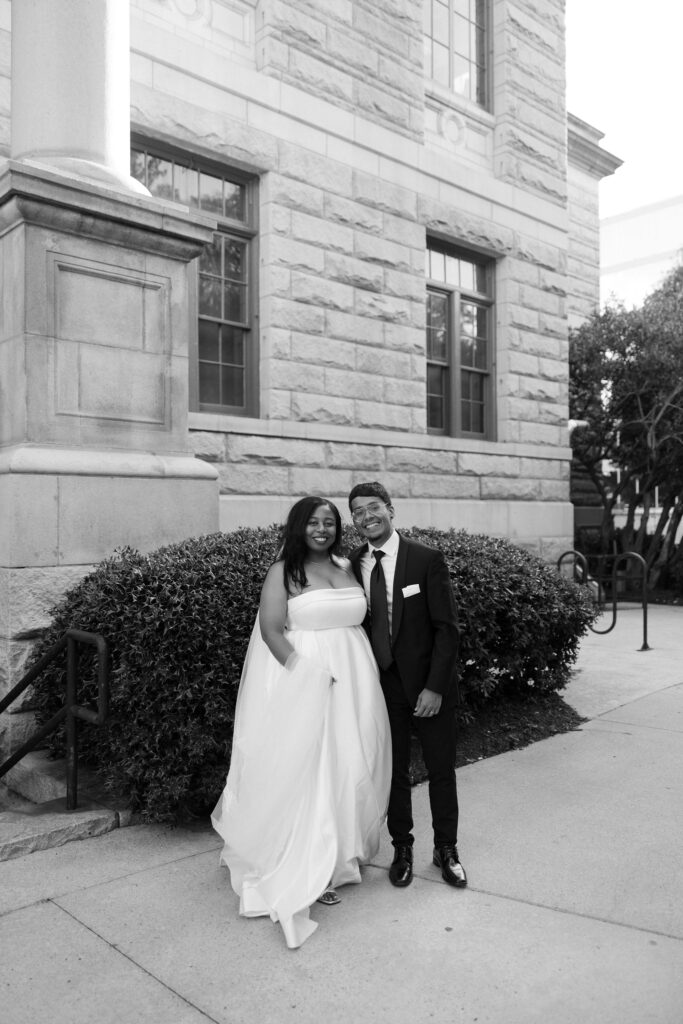 Black and white photo of a bride and groom posing outside of Historic DeKalb Courthouse