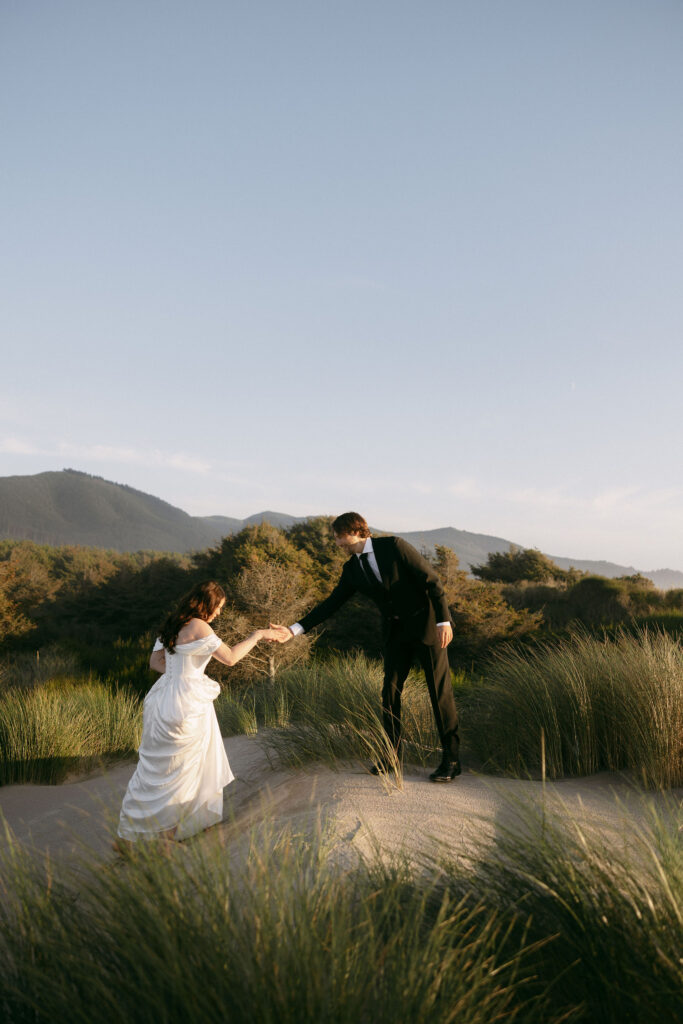 Man helping his wife walk up the beach during their Northern Oregon coast elopement