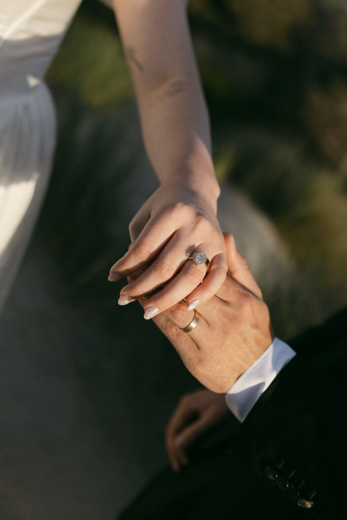 Couple holding hands and showing off their wedding rings on the beach