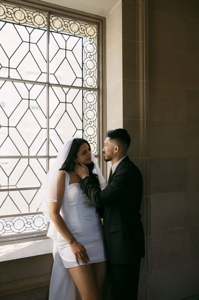 Couple posing by the large windows at San Francisco City Hall for their engagement photos