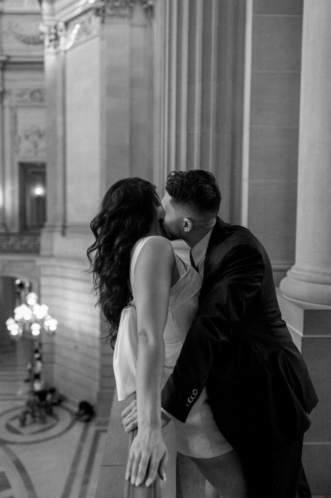 Black and white photo of a man kissing his fiancés neck during their San Francisco City Hall engagement photos