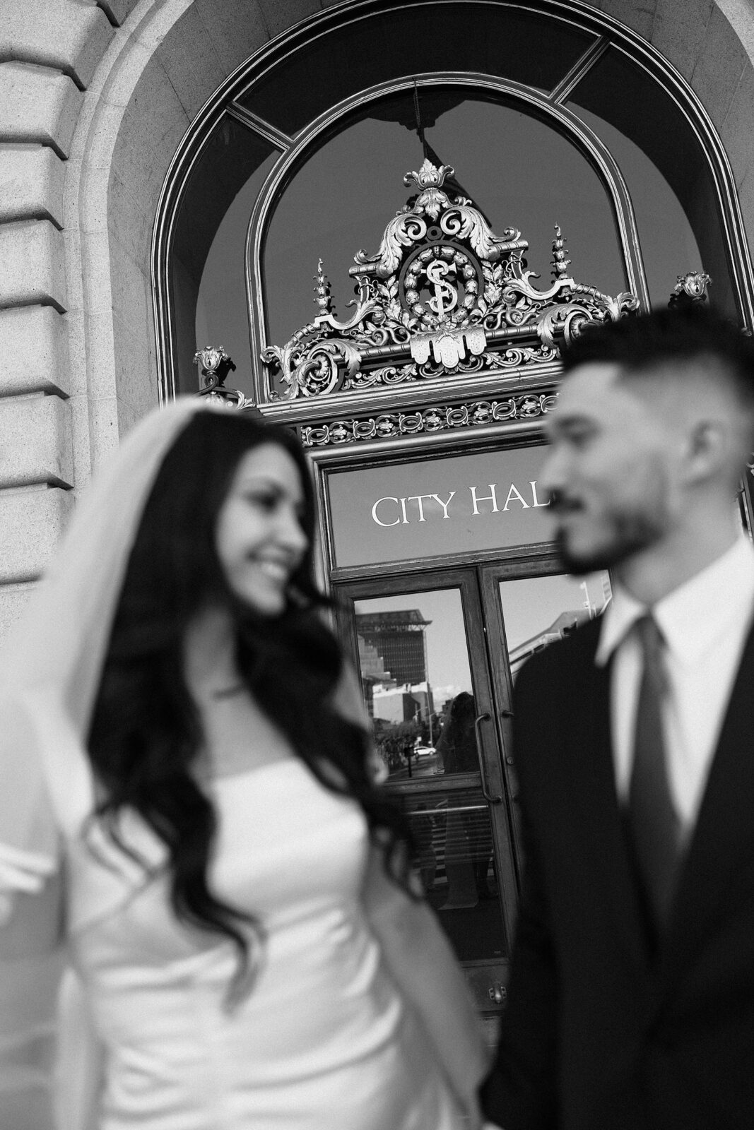 Black and white engagement photo of a couple posing in front of San Francisco City Hall